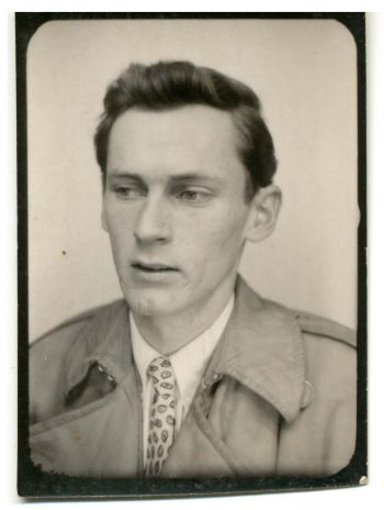 Head shot of William Gaddis circa 1955. Gaddis is wearing a jacket with sharply angled lapels and a spotted tie. 