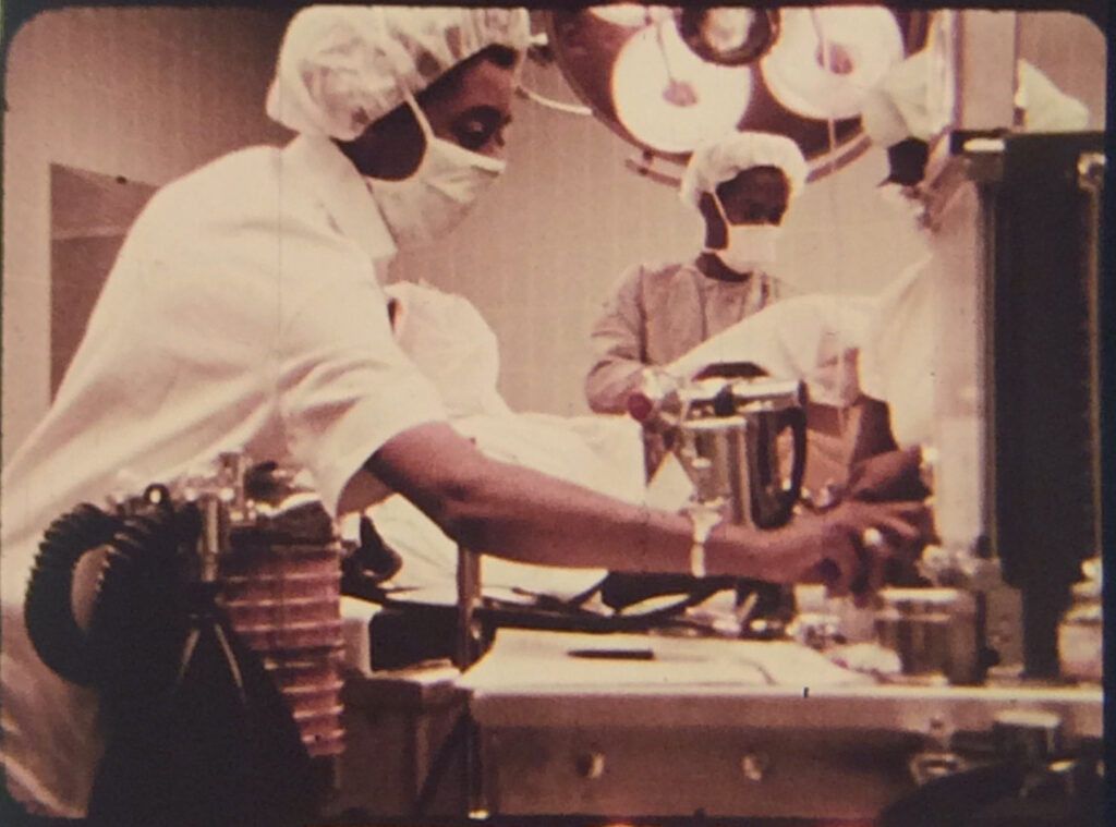 Still from "Code Blue" featuring three or more medical professionals with hairnets and surgical masks in an operating theater. 