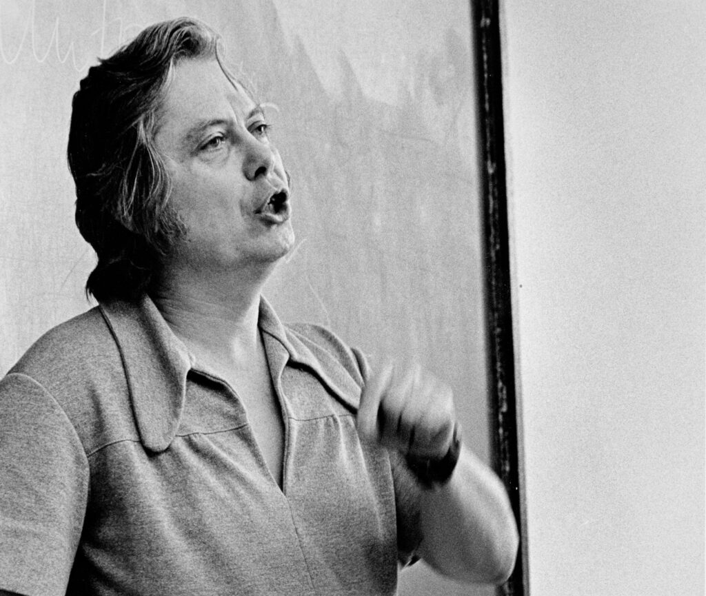 Action photo of William H. Gass speaking during a lecture. 