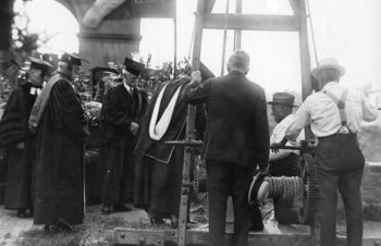 The photo shows that the 1923 ceremonial laying of the cornerstone of Duncker Hall was attended by four men in ceremonial robes, one in a nice suit and hat, and was lowered into the foundation by two workers in suspenders using a rope system. 