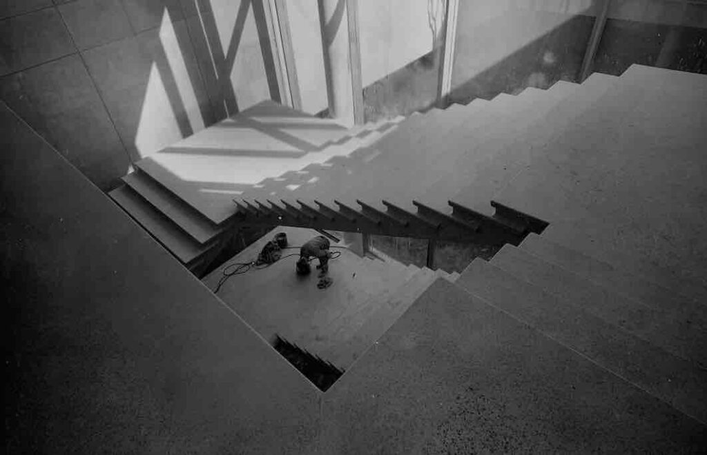 Construction shot of the Andrew and Jayne Kagan Grand Staircase. The cement is poured and the stairs are structurally sound in this photo, as demonstrated by the lone figure of a workman, but there are no railings or other finishing touches. 