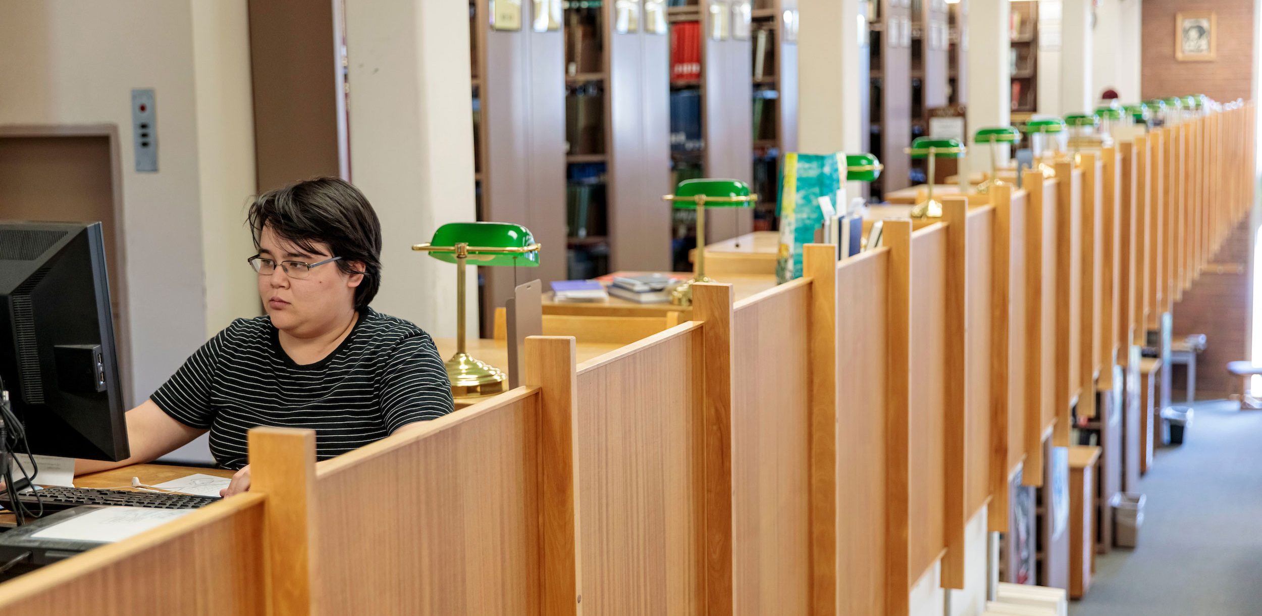 Student using a computer terminal near study cubbies in the Library book stacks.