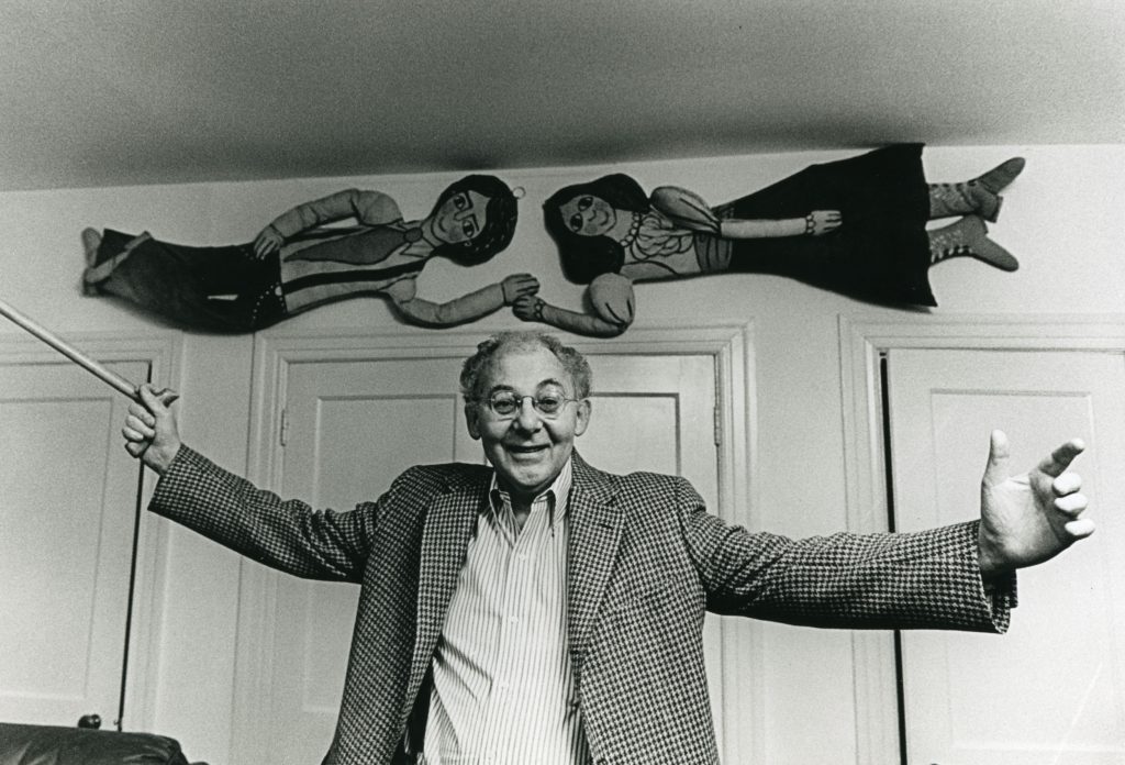 A man standing beneath a pair of puppets mounted to a wall.