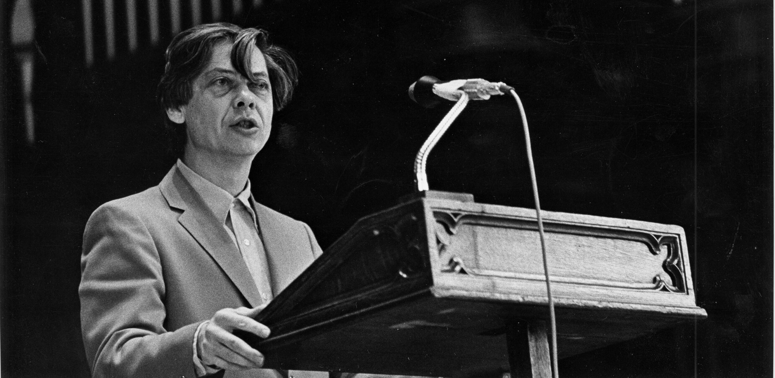 William H. Gass giving a speech at a podium.