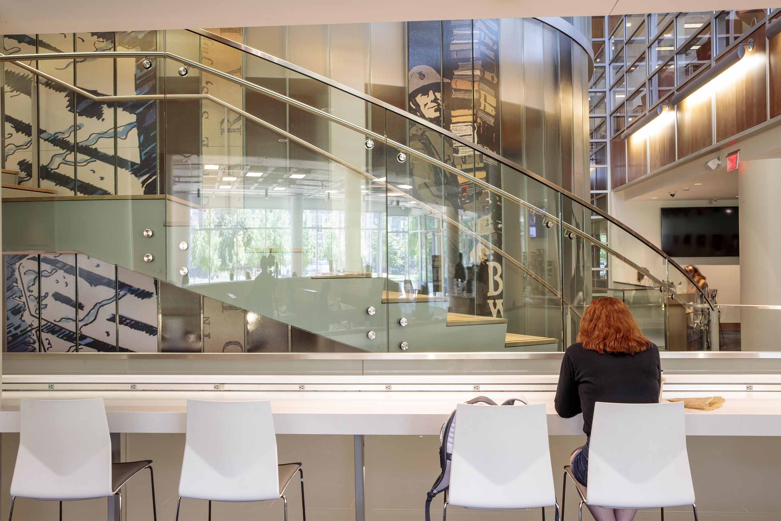 A student studies at the bar seating area of Whispers Cafe with a view of the Newman Tower stairs in the background.