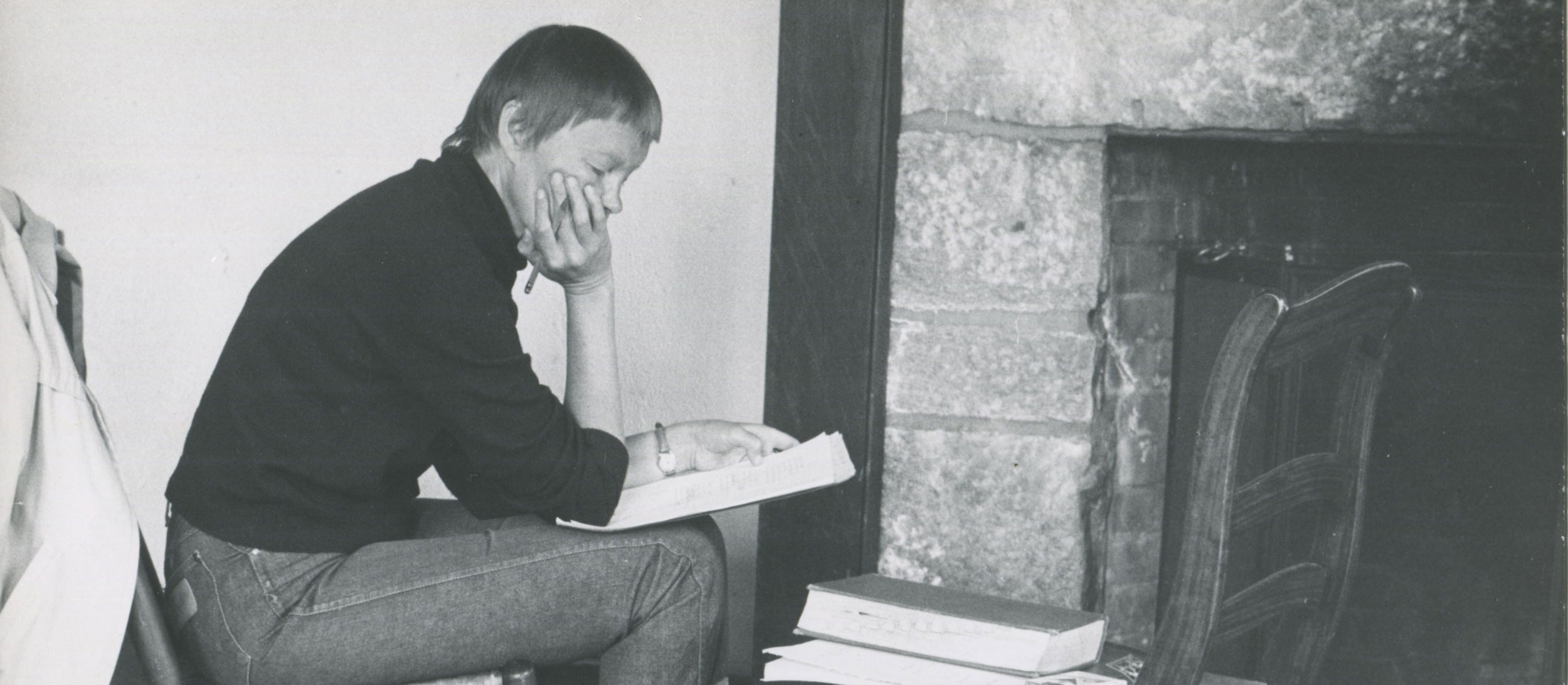 A candid photo of May Swenson as she studies a manuscript in front of a fire.