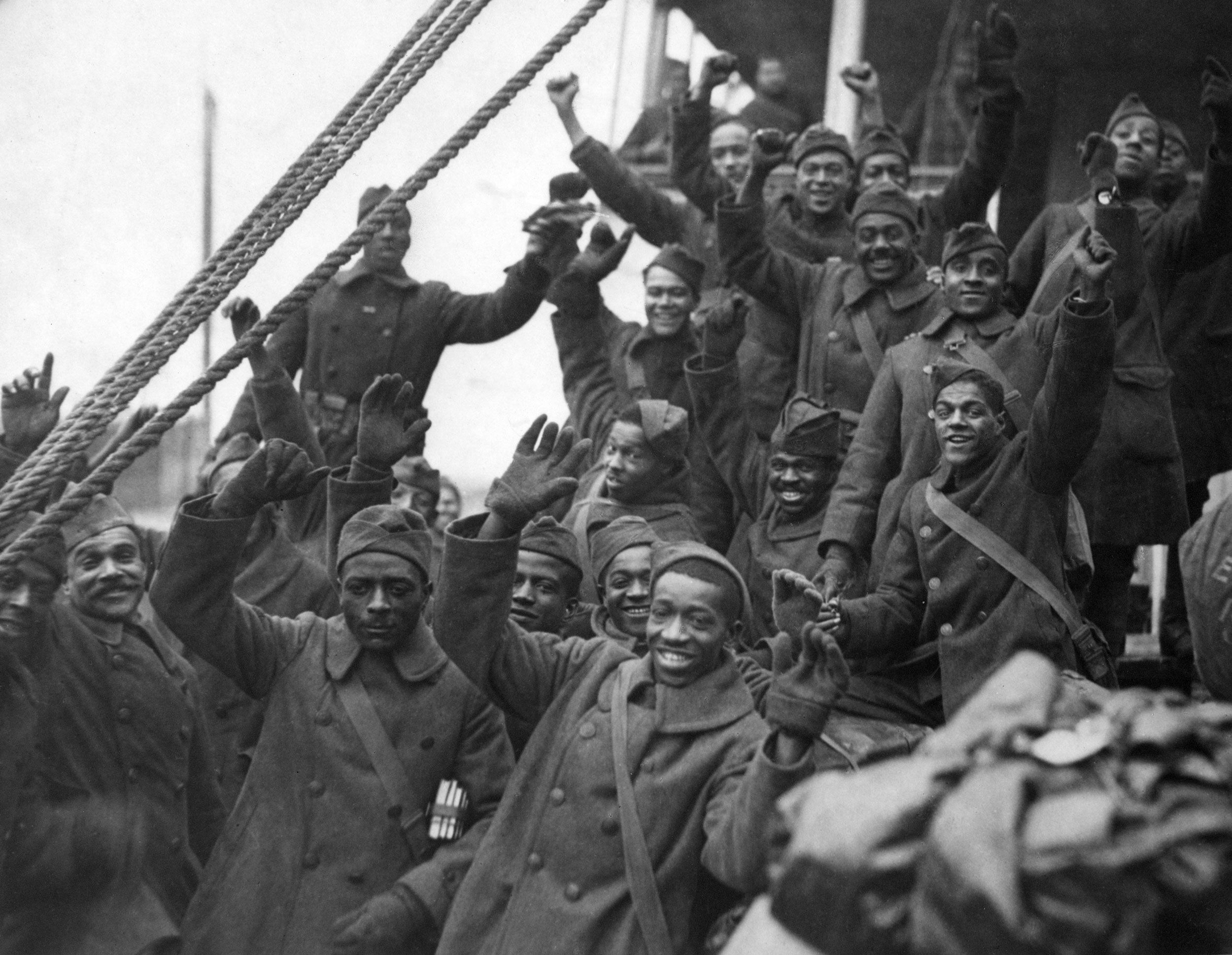 The Harlem Hellfighters in peacoats with arms raised in a cheer.