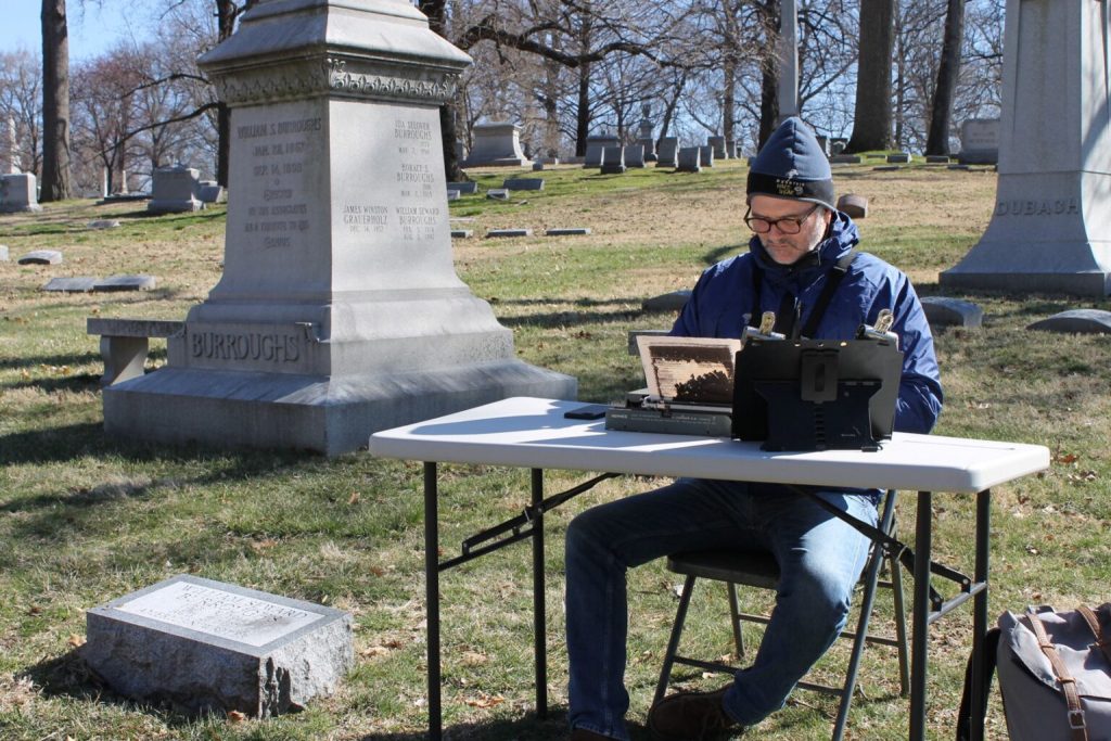 Tim Youd in Bellefontaine Cemetery sitting at a collapsable table and chair retyping Naked Lunch. 