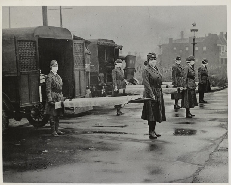 Female volunteers with the St. Louis Red Cross on duty, Oct. 1918, during the influenza epidemic. (Library of Congress, LC-DIG-ds-01290). In the photo, four teams of nurses in uniform with surgical masks covering their faces stand at the ready on either end of stretchers.