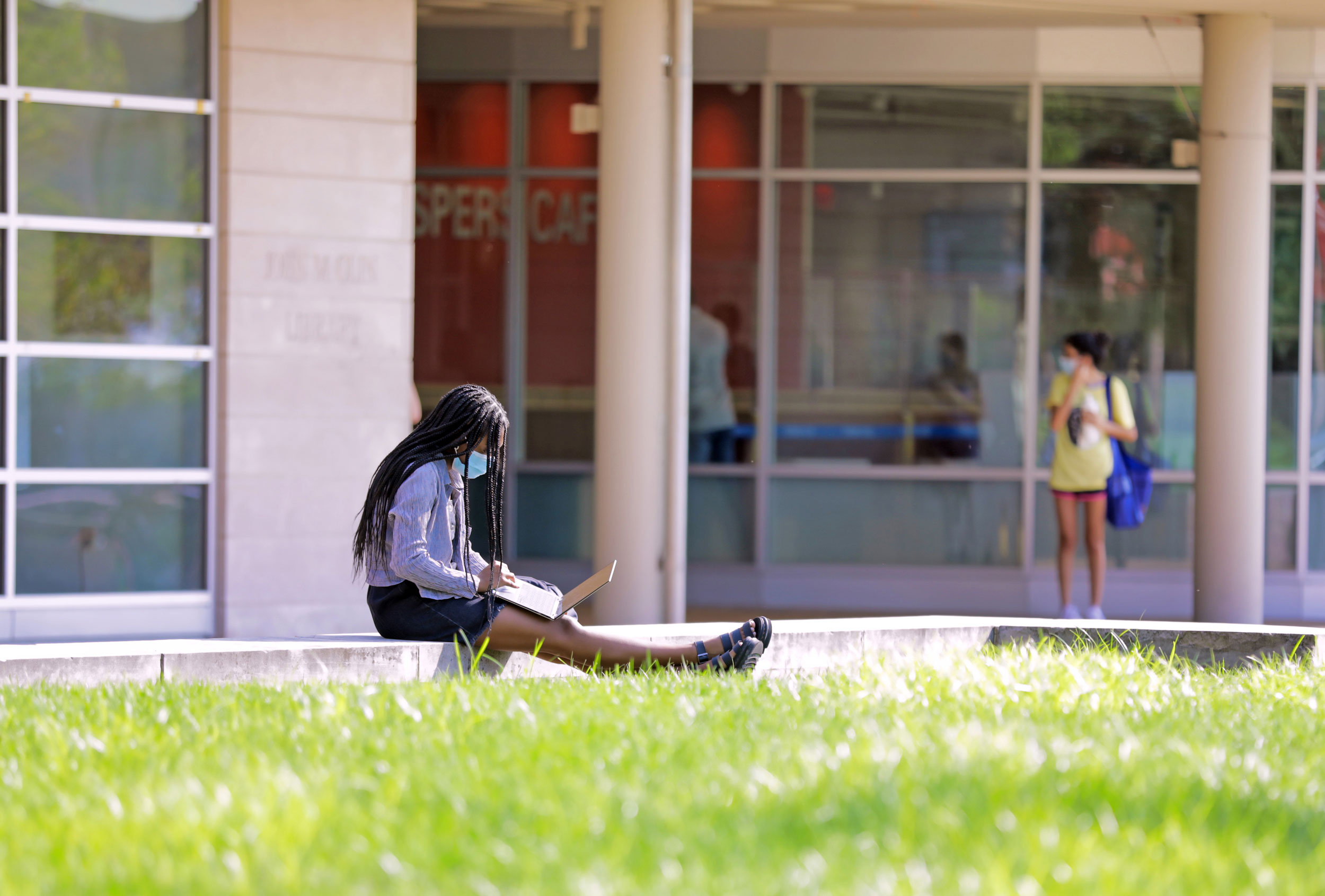 A student sitting and working on their laptop while masked outside of Olin Library.