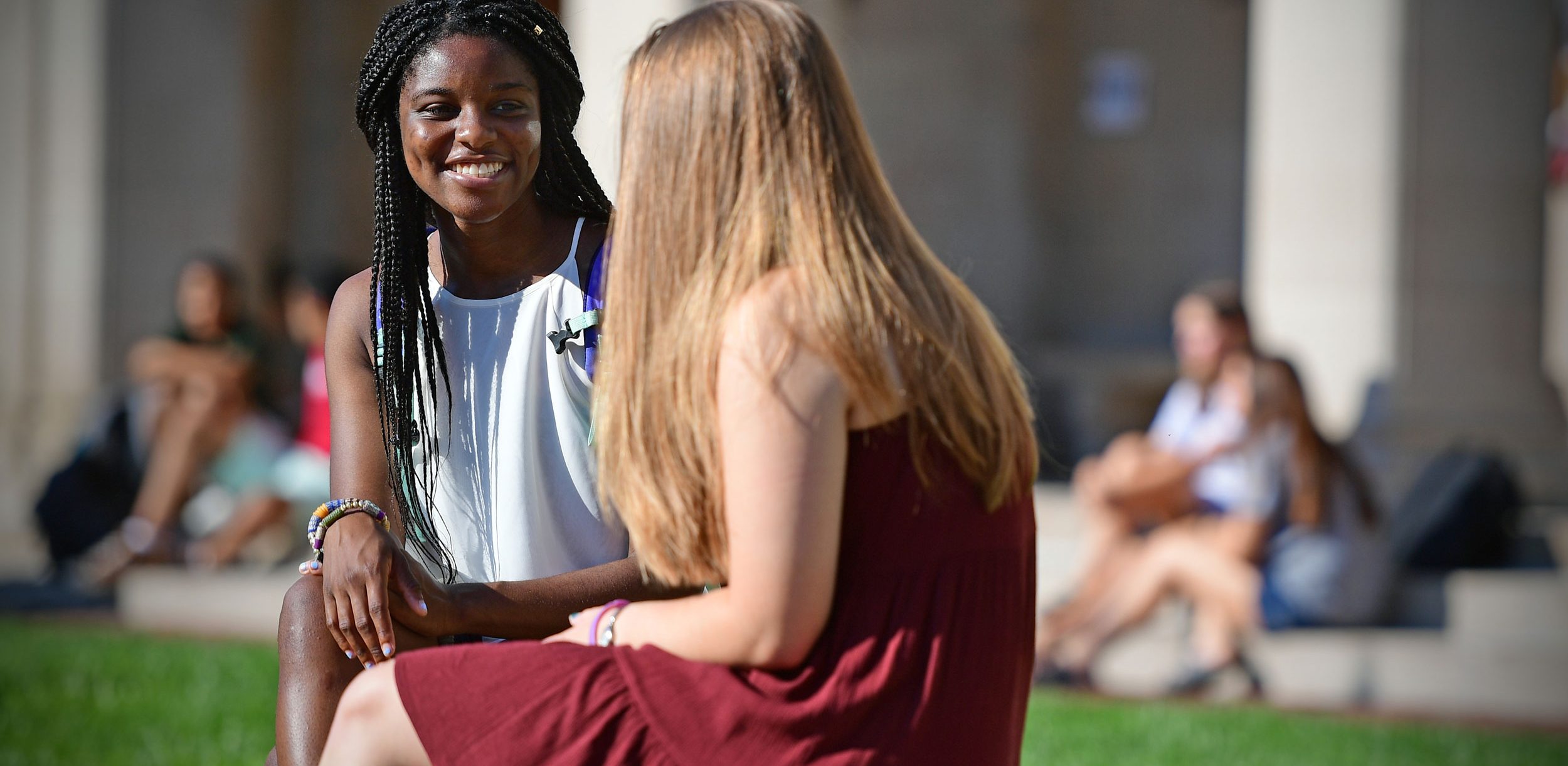 Two female presenting students talking at a bench on campus.