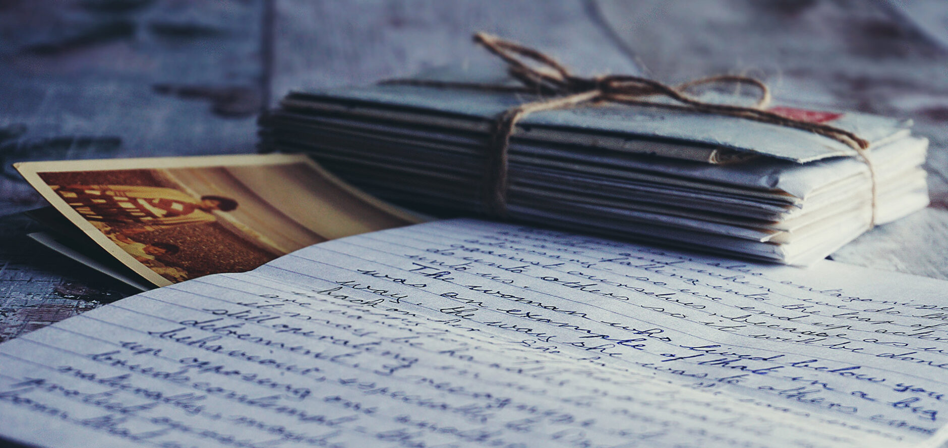 A photo of multiple envelopes tied with twine sitting on top of an older, sepia-toned photograph and a handwritten letter. The angle of the letter does not permit reading.