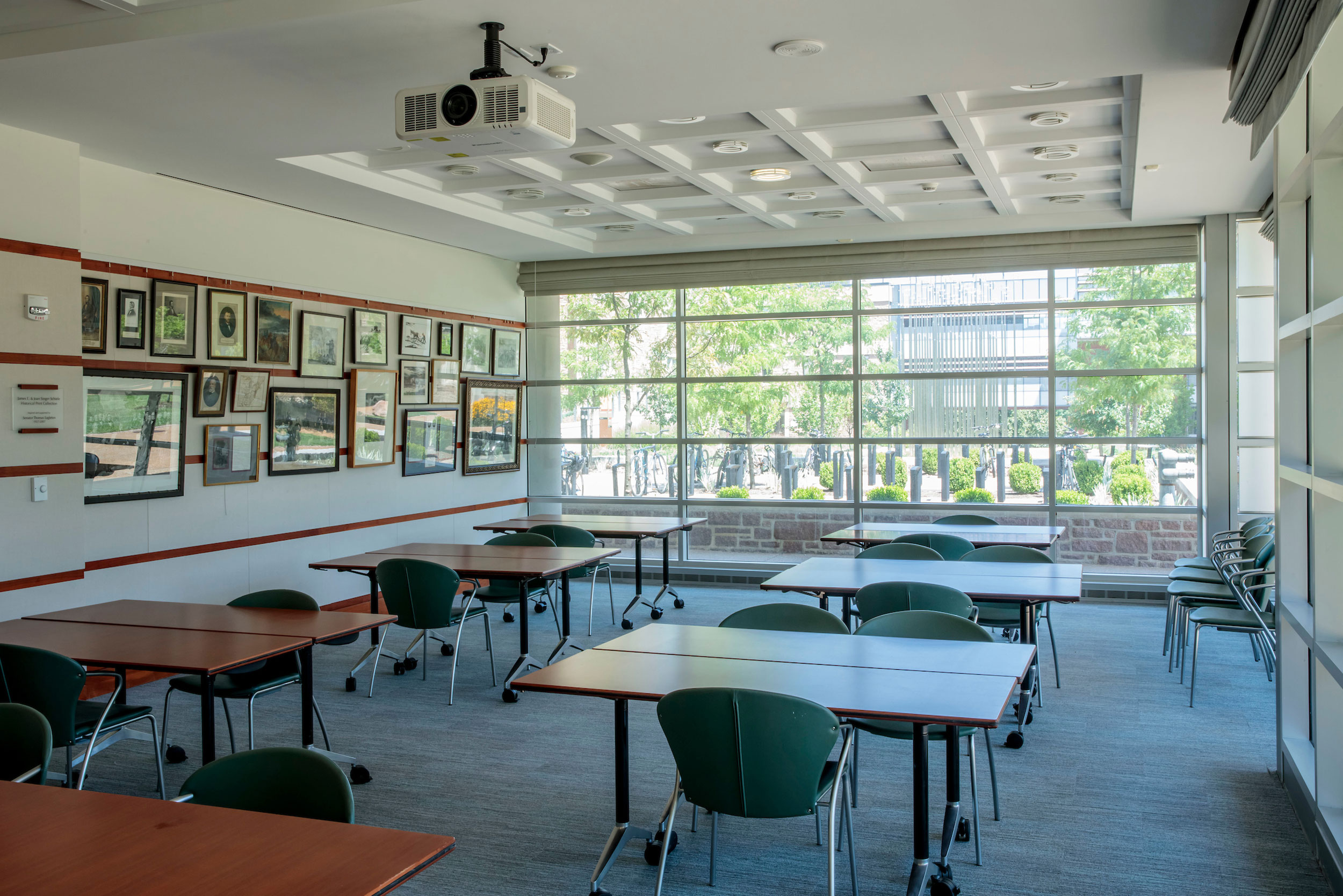 The Mendle Classroom has smaller, two-person tables and hosts a projector within the room. The space itself is large with many of the walls featuring ceiling windows.