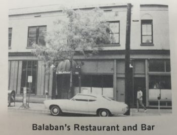 Two-story shopfront nestled amongst other shopfronts along a street. 