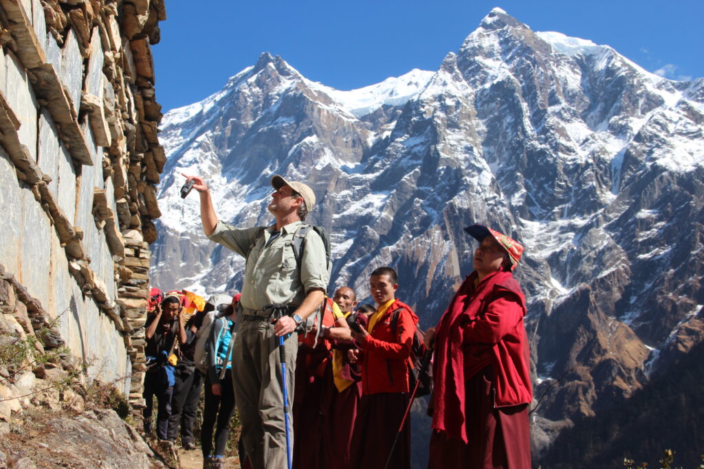 Anthropology Professor Geoff Childs and others on a backpacking expedition around the Himalayas with Buddhist monks wearing traditional red robes accompanying them.