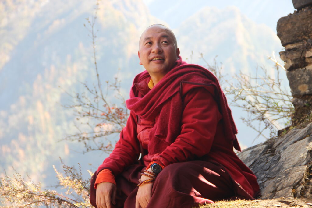 A Buddhist monk sits on a mountain path in traditional red robes.