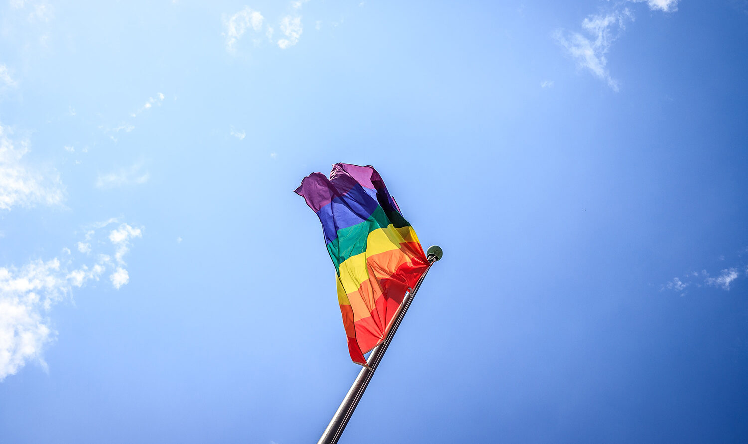 Rainbow pride flag being flown against the background of a crisp blue sky.