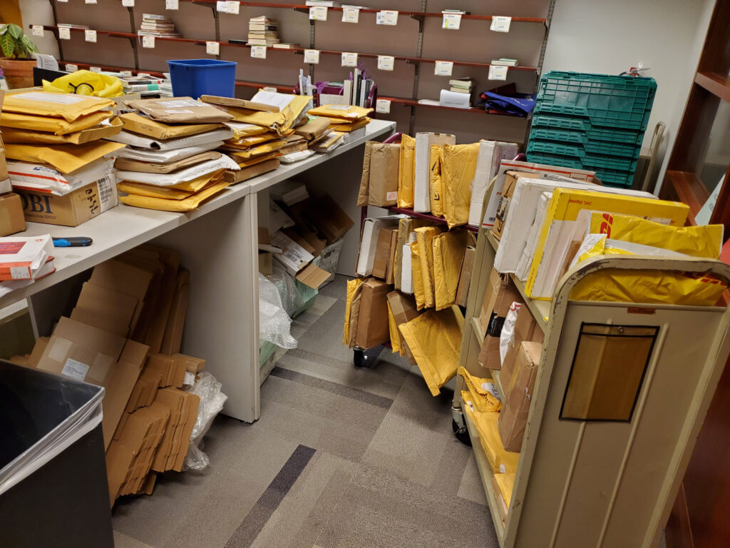 Hundreds of unopened package sleeves sit stacked together on book carts and counter-space.