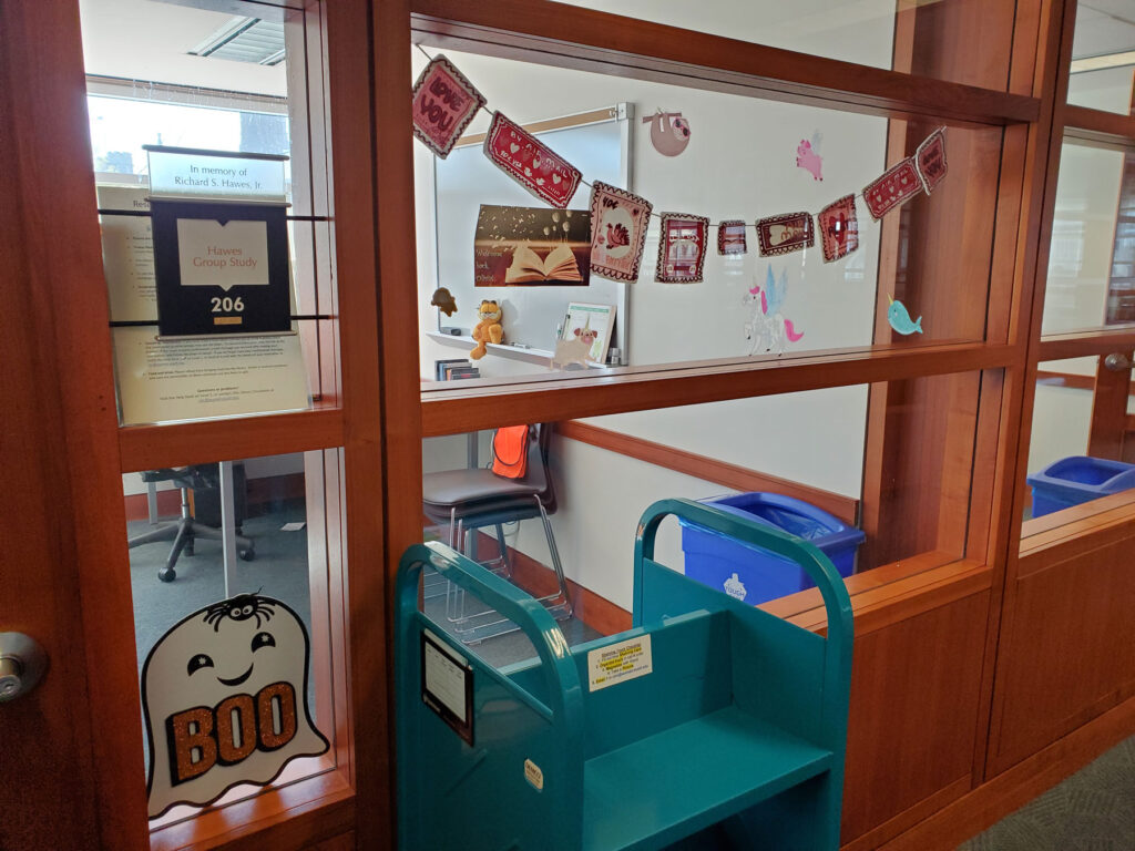 Cute banners and window clings decorate the interior window of an office. The window clings show a winged unicorn, a pig with wings, and a narwhale.