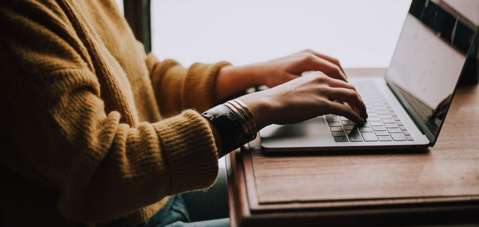 Student sitting indoors with a laptop at a wooden desk.