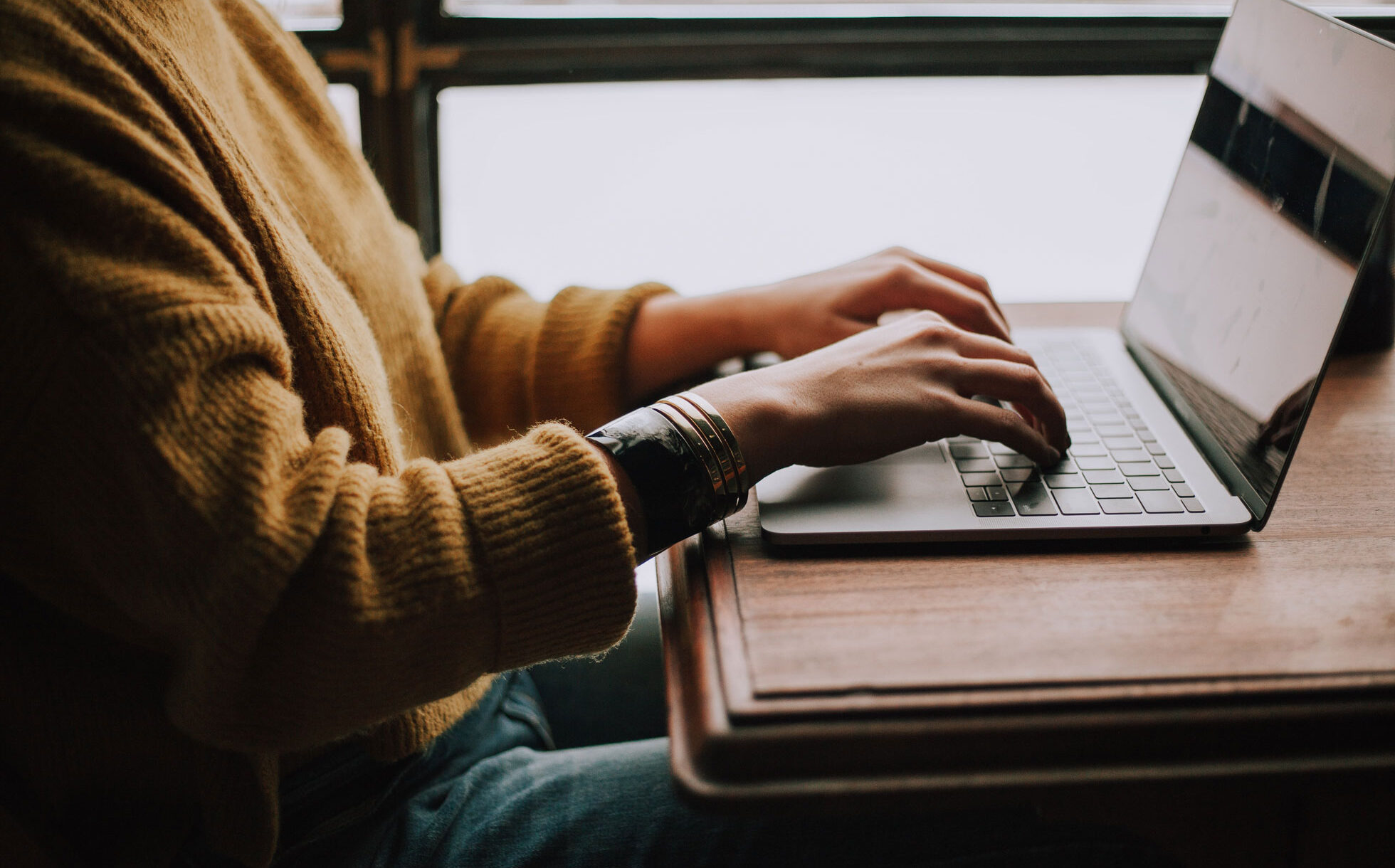 Student sitting indoors with a laptop at a wooden desk.