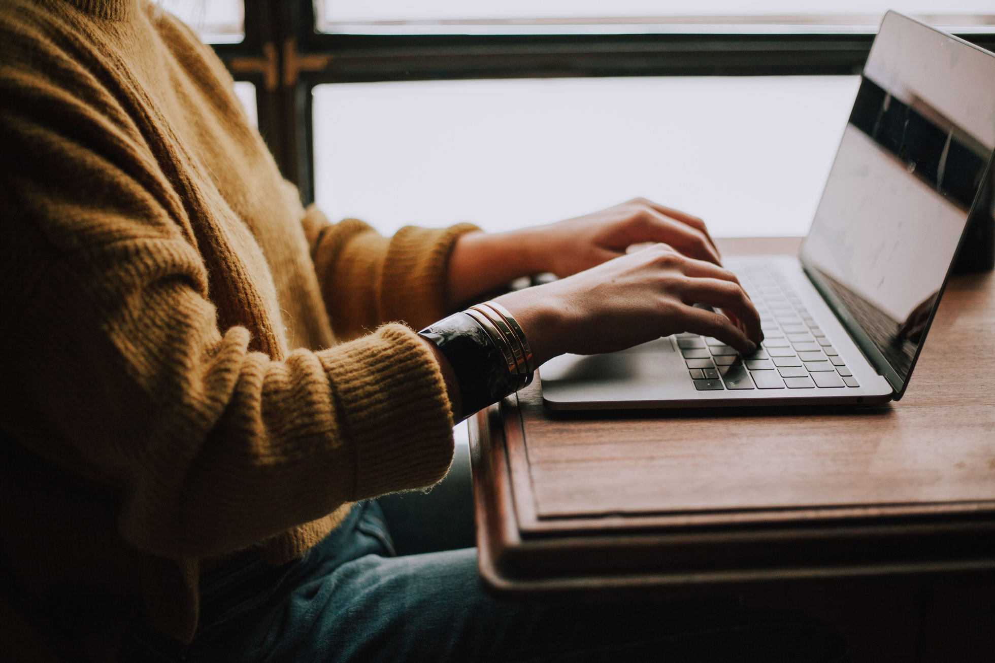 Student sitting indoors with a laptop at a wooden desk.