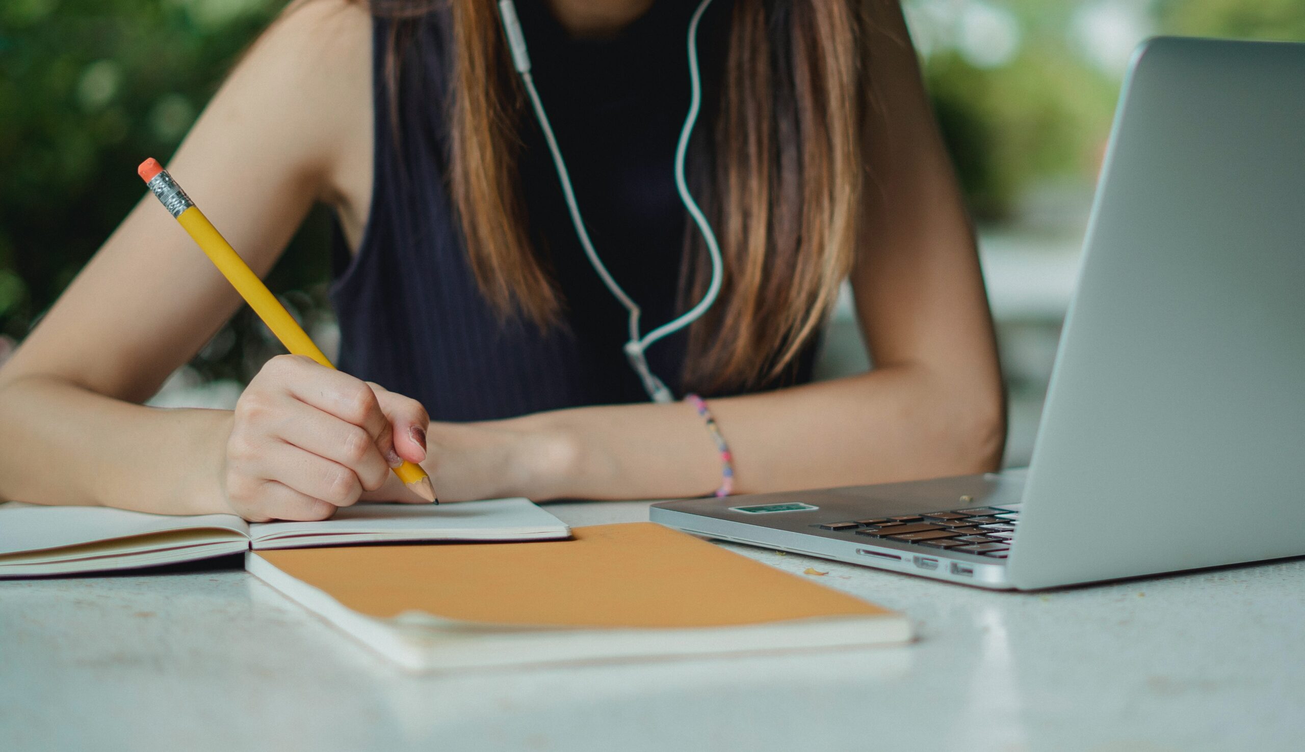 Stock image of a student seated in front of a laptop writing notes.