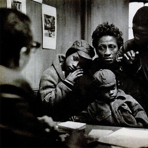 A mother with children looks into the camera from behind a service desk.