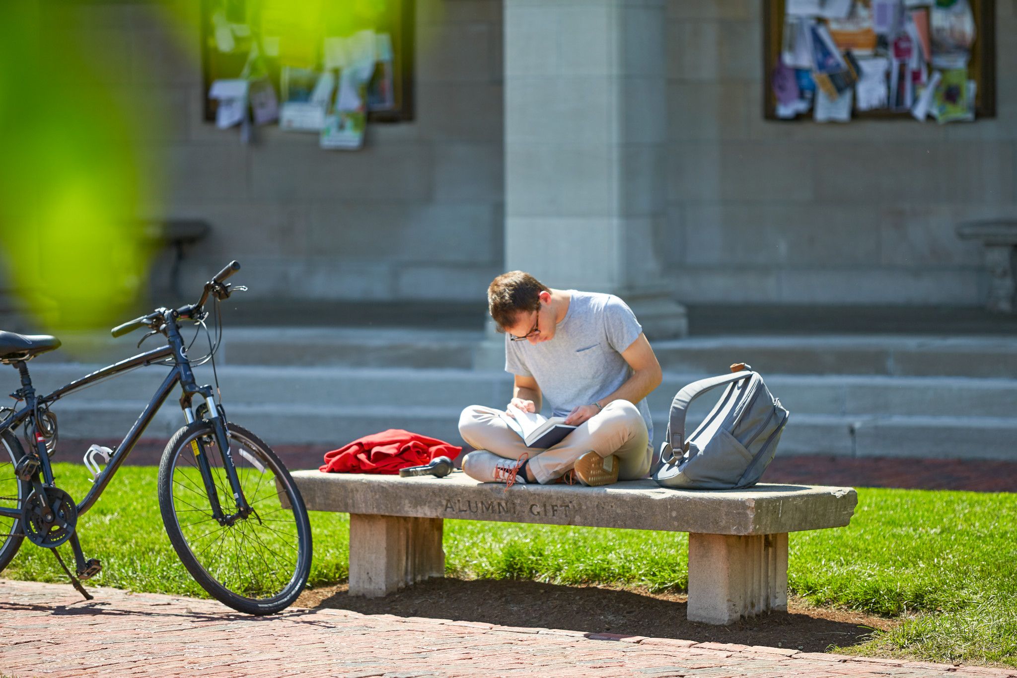 A student engrossed in a book while sitting on one of the stone benches around campus.