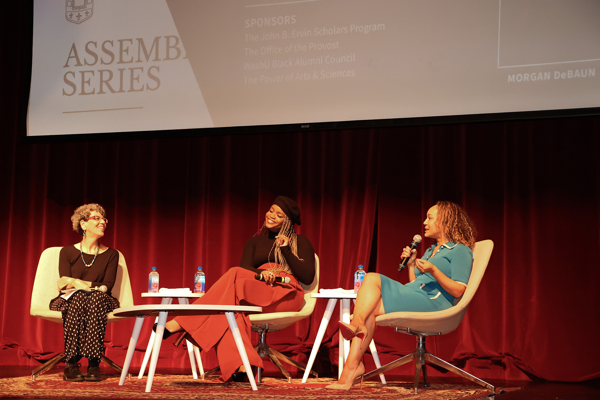 Three speakers sitting on chairs on the stage.