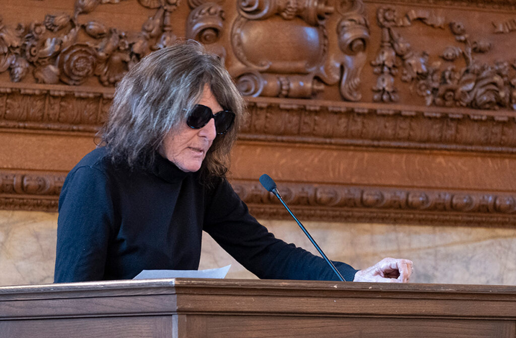 Woman wearing sunglasses reading behind a lectern