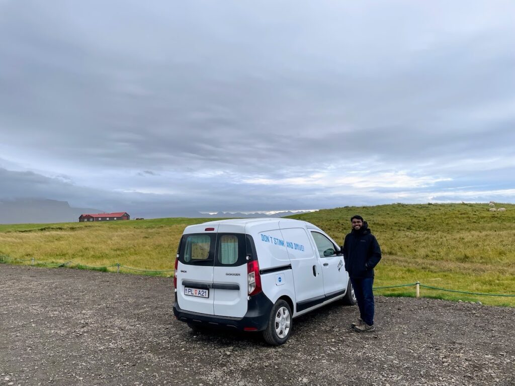 Person standing by camper van in front of a green pasture.