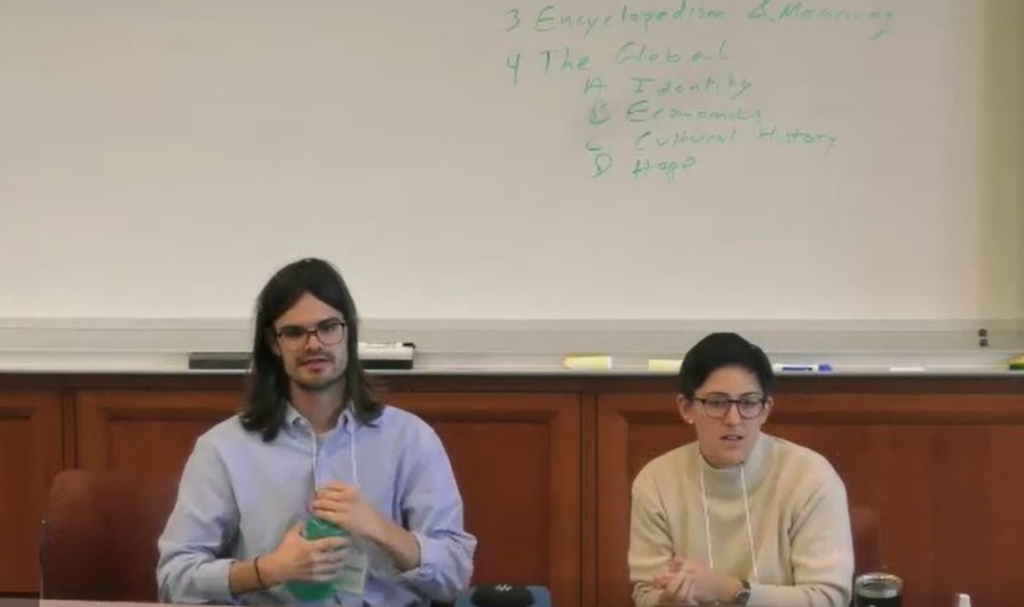 Two people sitting and discussing in front of a whiteboard.