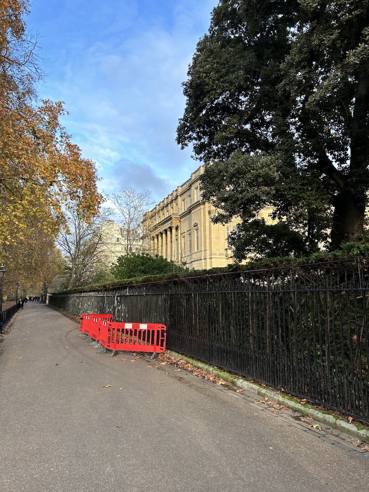 Black iron fence in front of a mansion with trees within and outside the fence.