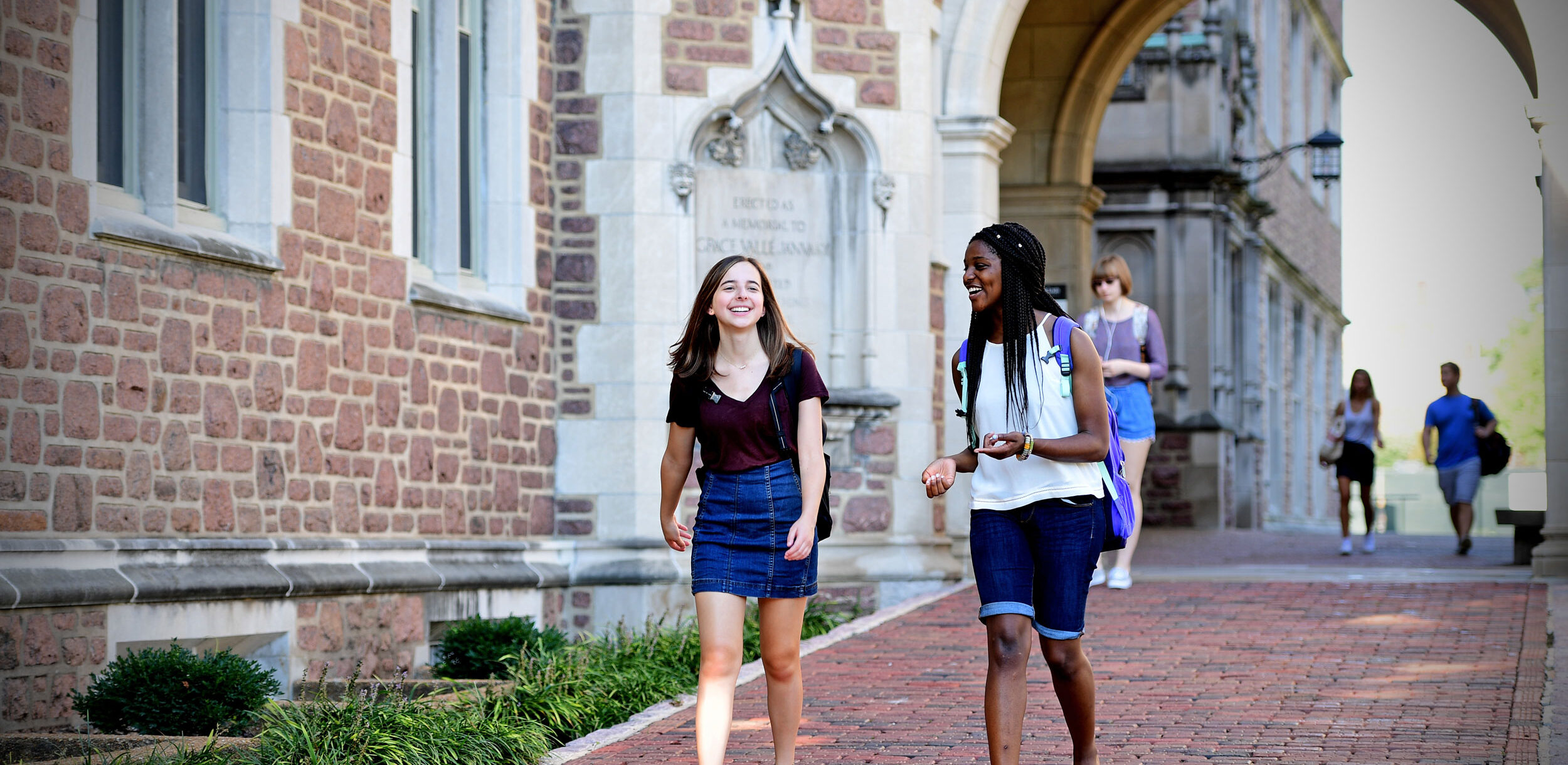 Two students walking on a campus path while chatting.