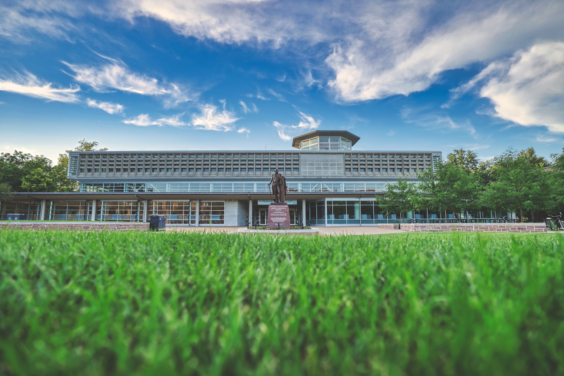 Grassy lawn under a blue sky with the statue of George Washington and Olin Library in the background.