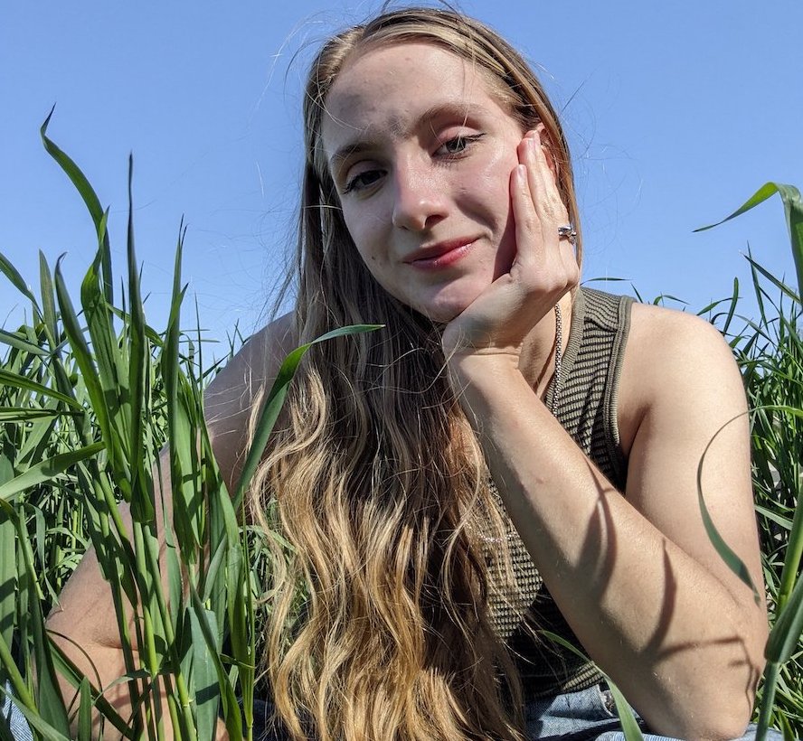 A woman sitting amid green crops in a field.