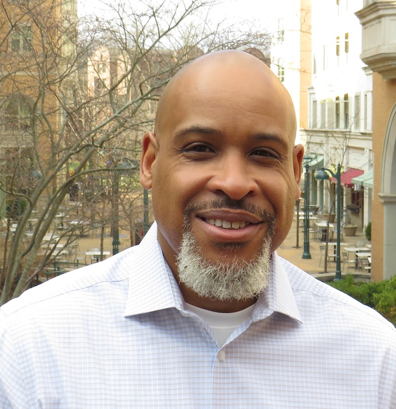 Headshot of a man with trees and buildings in the background.