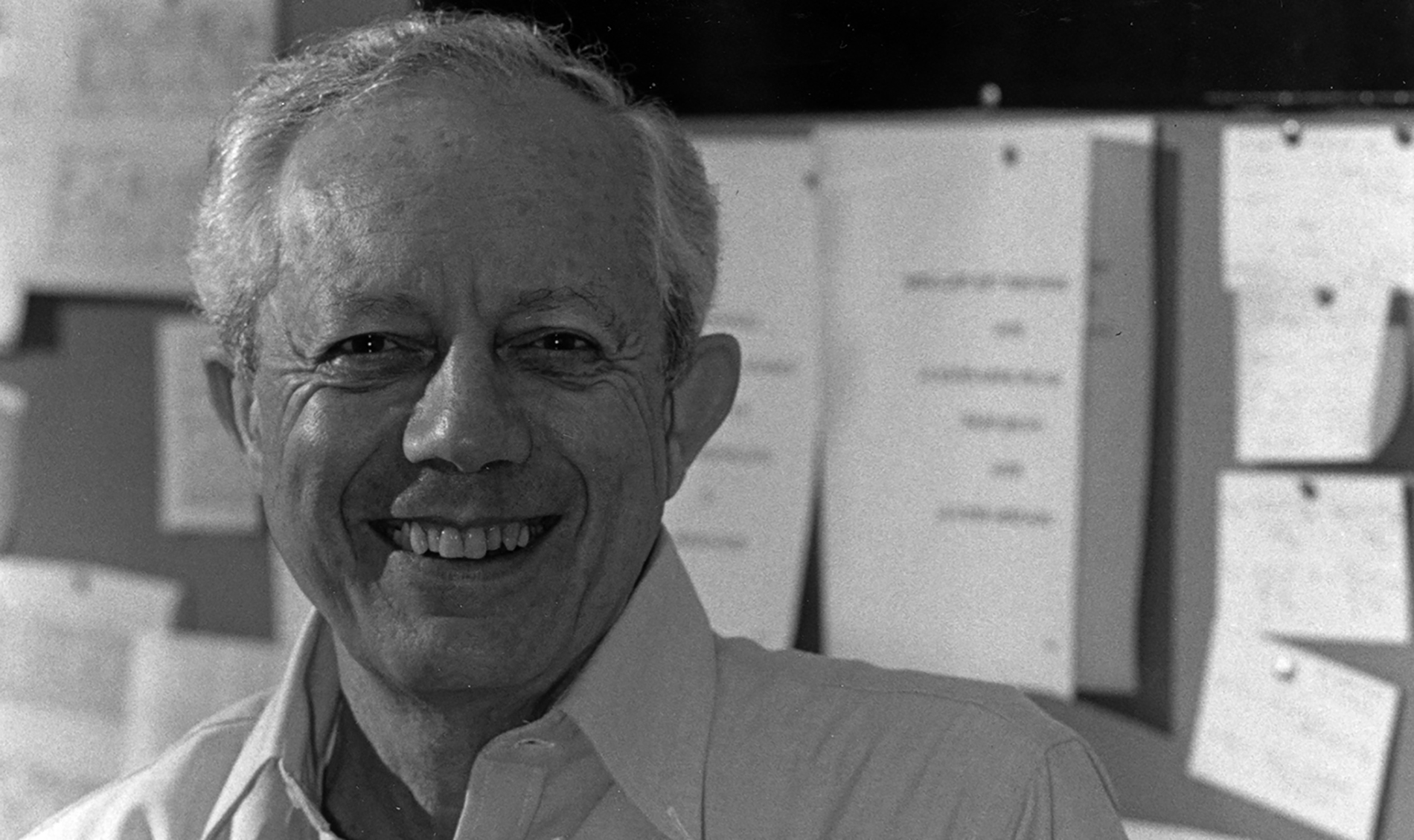 Professor Michael W. Friedlander is smiling at the camera in front of a backdrop of pinned notecards and papers.