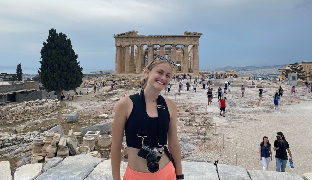 A woman standing in front ruins and a columned structure.