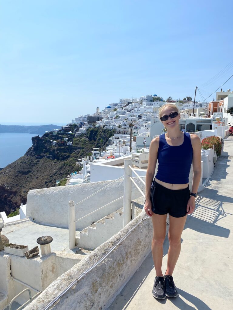 Woman standing on a street overlooking the ocean and white buildings.