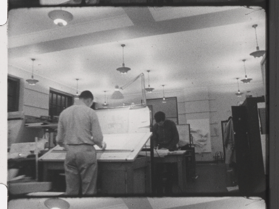 B&W photo of people working on architectural layouts