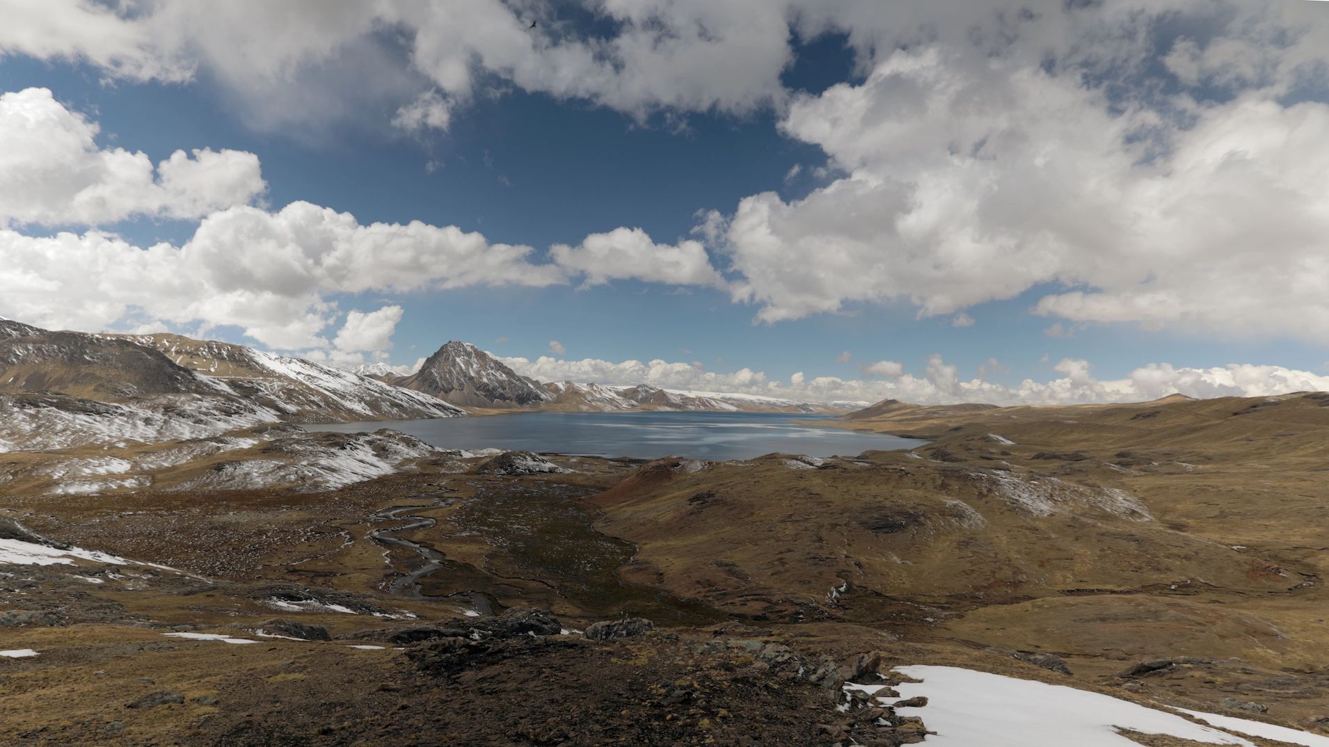 A landscape of a lake surrounded by land with clouds on top.