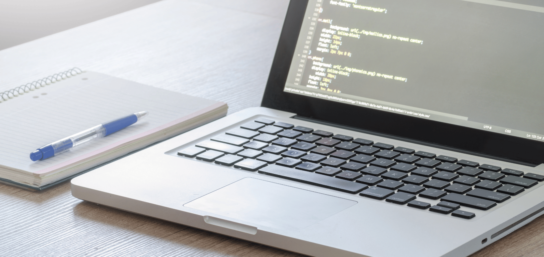 Laptop with code next to a pad of paper