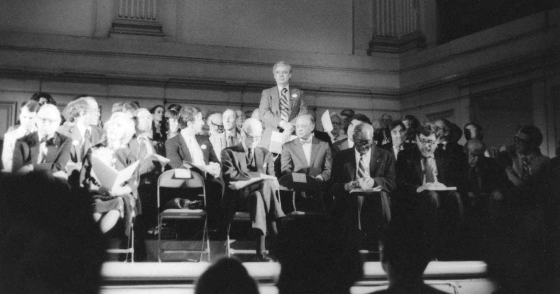 William H. Gass standing amongst a seated crowd.