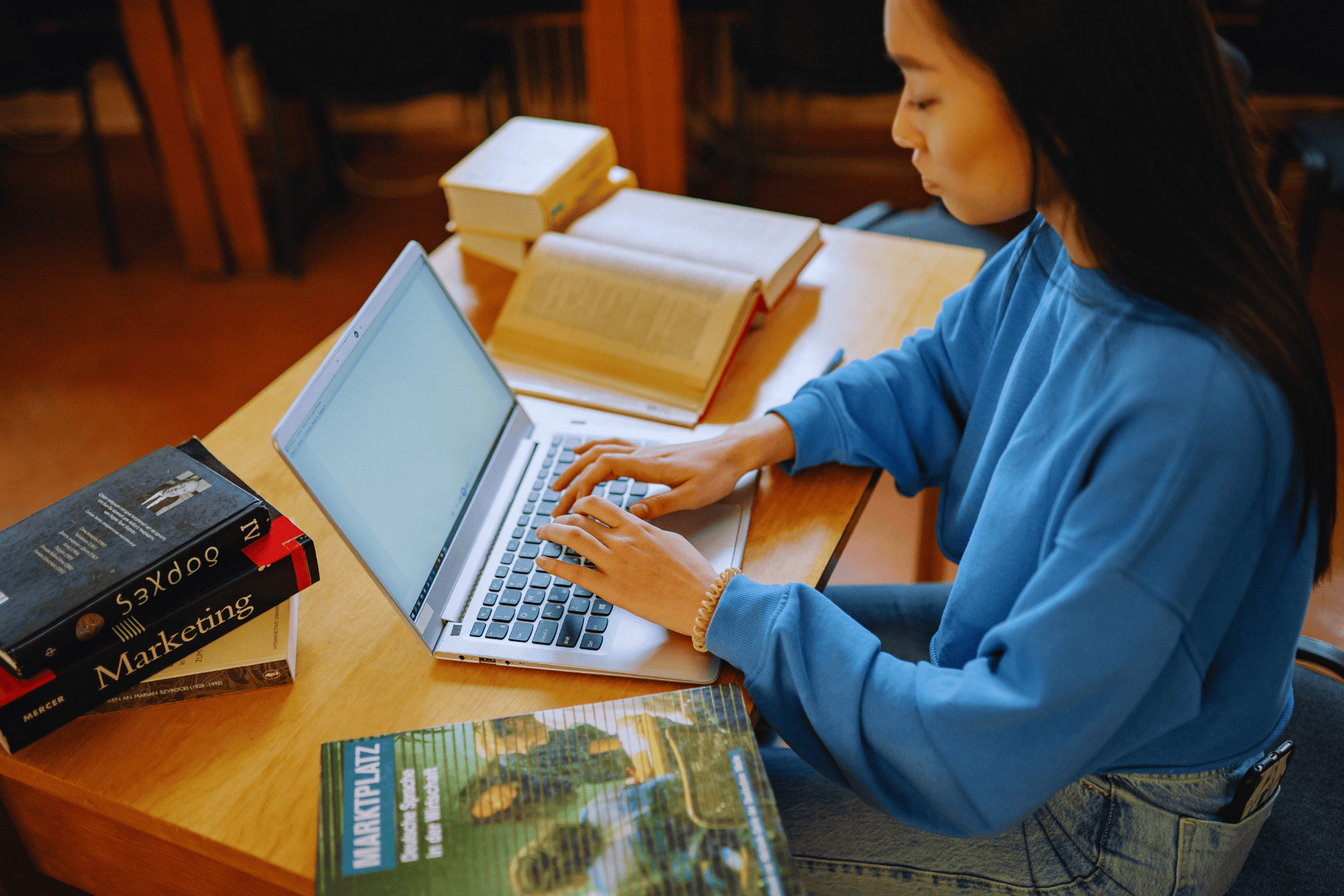 Stock photo of student typing on laptop with stack of books