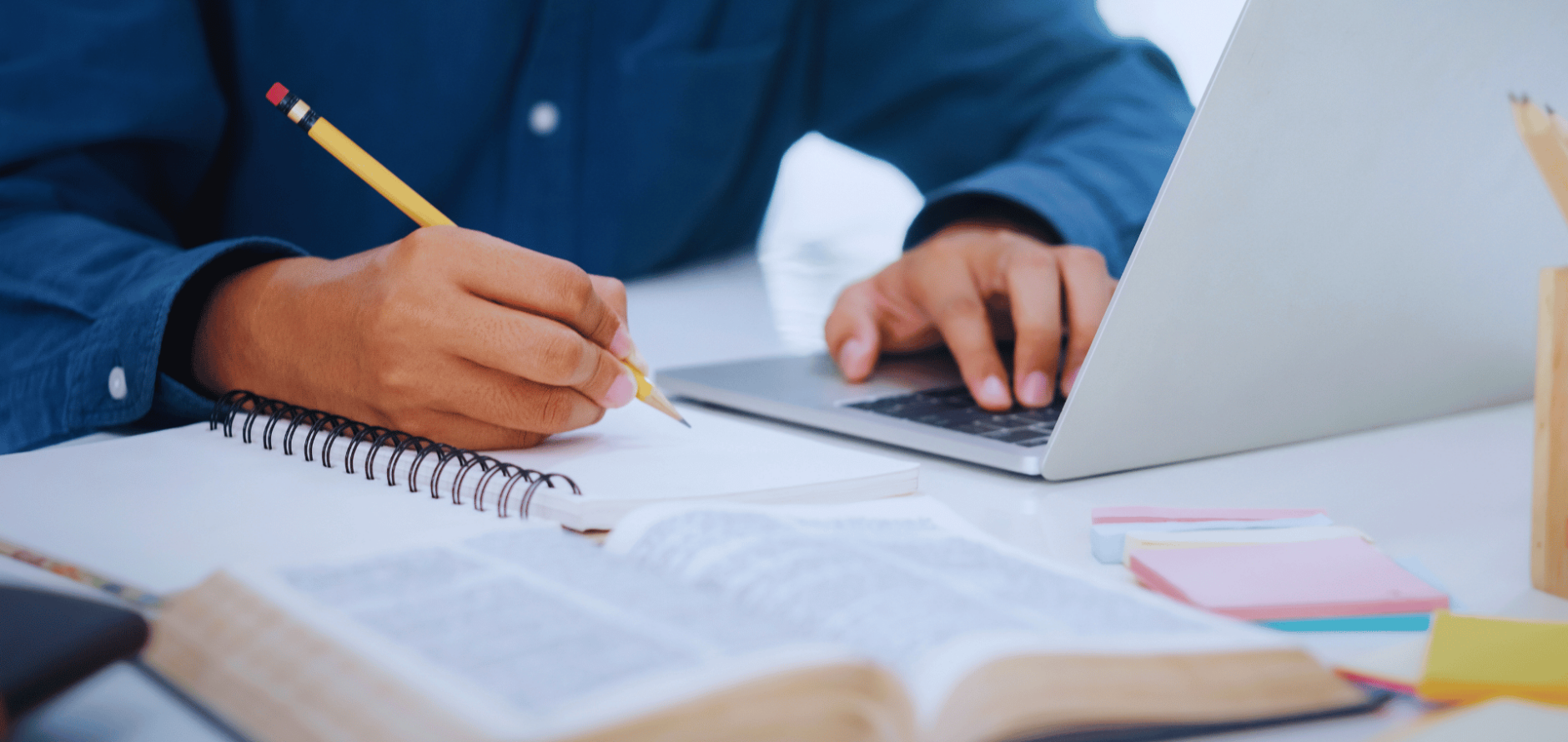 Stock image of person taking notes in notebook and scrolling on laptop