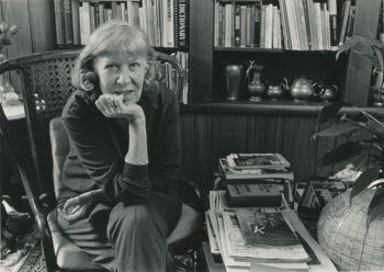 A woman seated in front of a bookshelf.