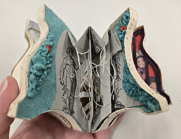 The inside of a movable miniature book filled with origami, string, and other elements to enable movement.