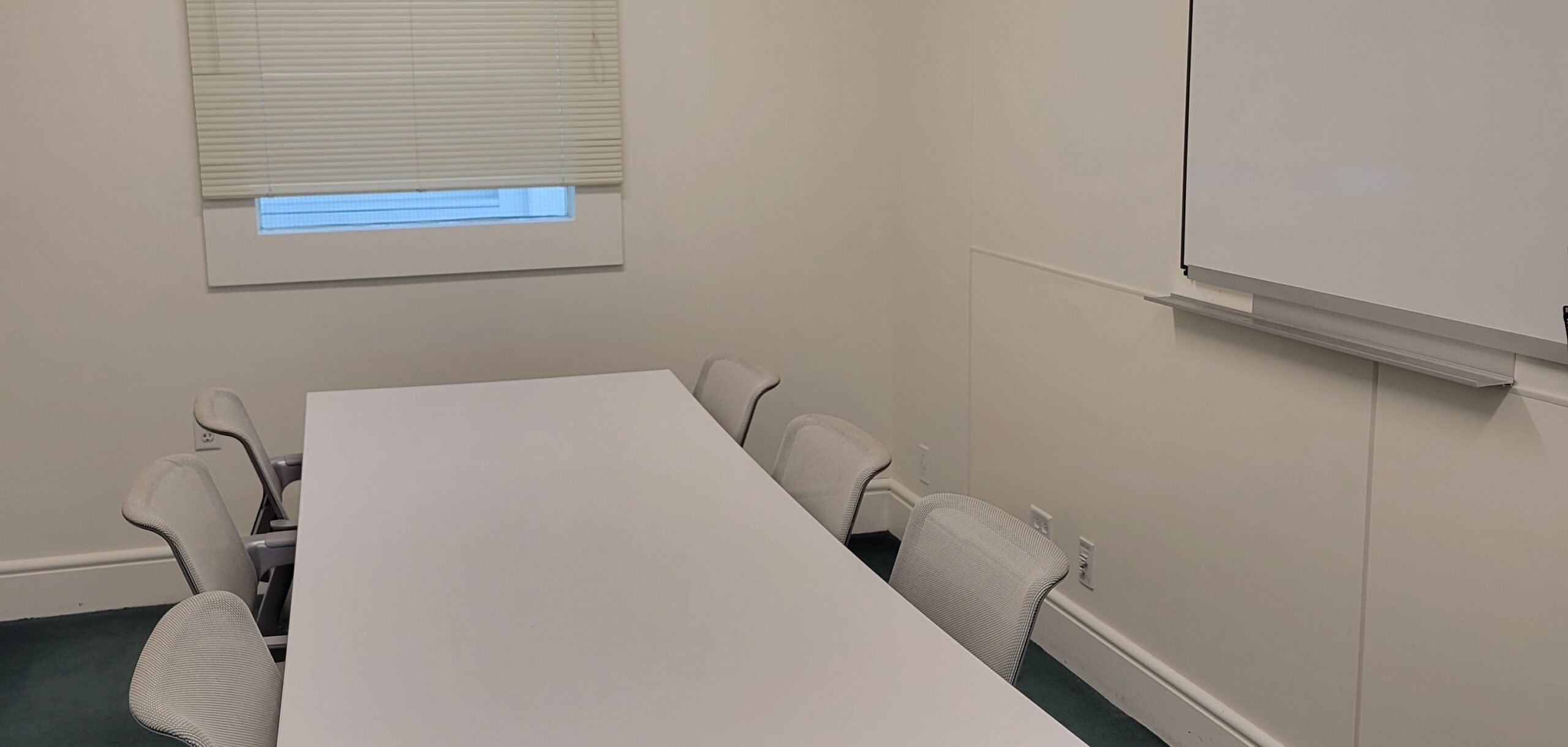 A small study room with a white table and four chairs, there is a whiteboard on one wall.